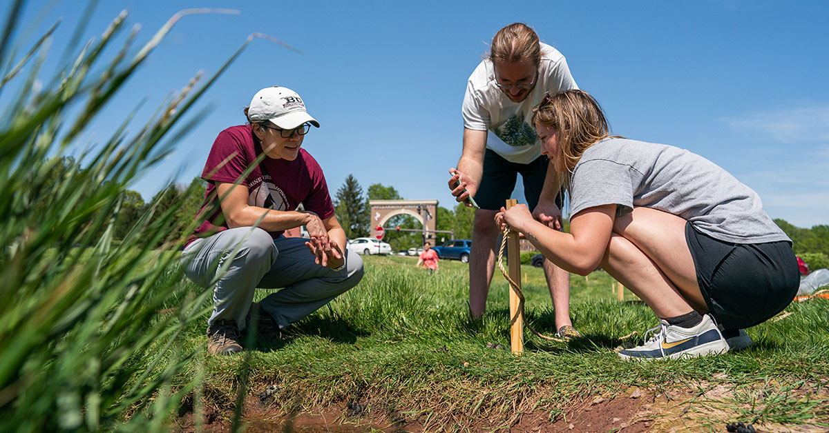 three people kneeling in the grass on campus at Bellarmine