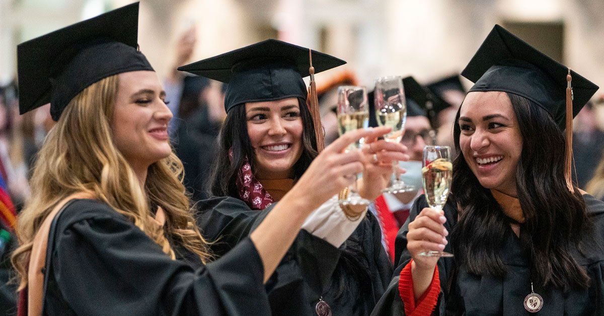 Three students in caps and gowns toasting with Champagne 
