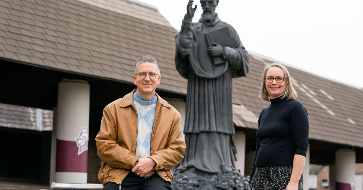 Christopher Graney, an adjunct scholar at the Vatican Observatory, and Dr. Kate Bulinski, associate professor of Geosciences, pose in front of the St. Robert Bellarmine statue on Bellarmine's campus.