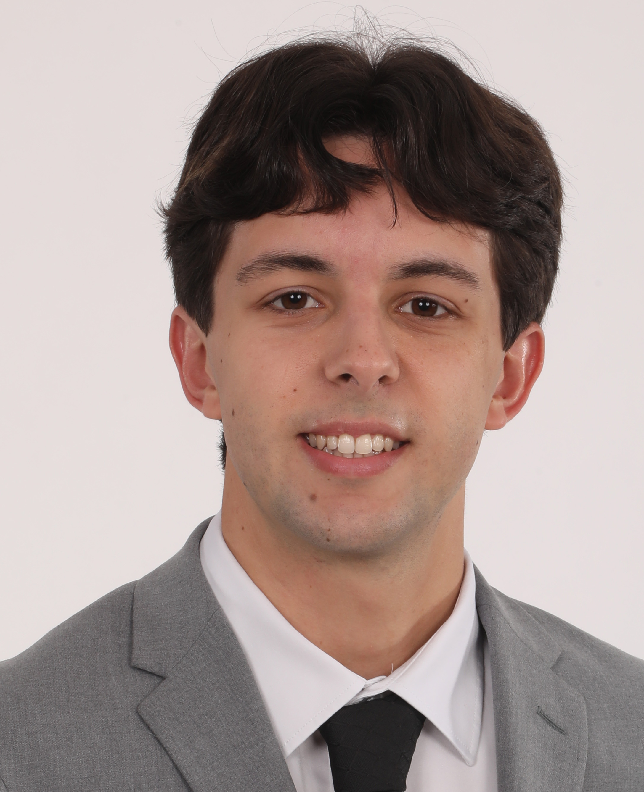 Portrait of a young man in a gray suit, white shirt, and black tie against a plain light background