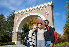 students pose for a photo in front of the arch